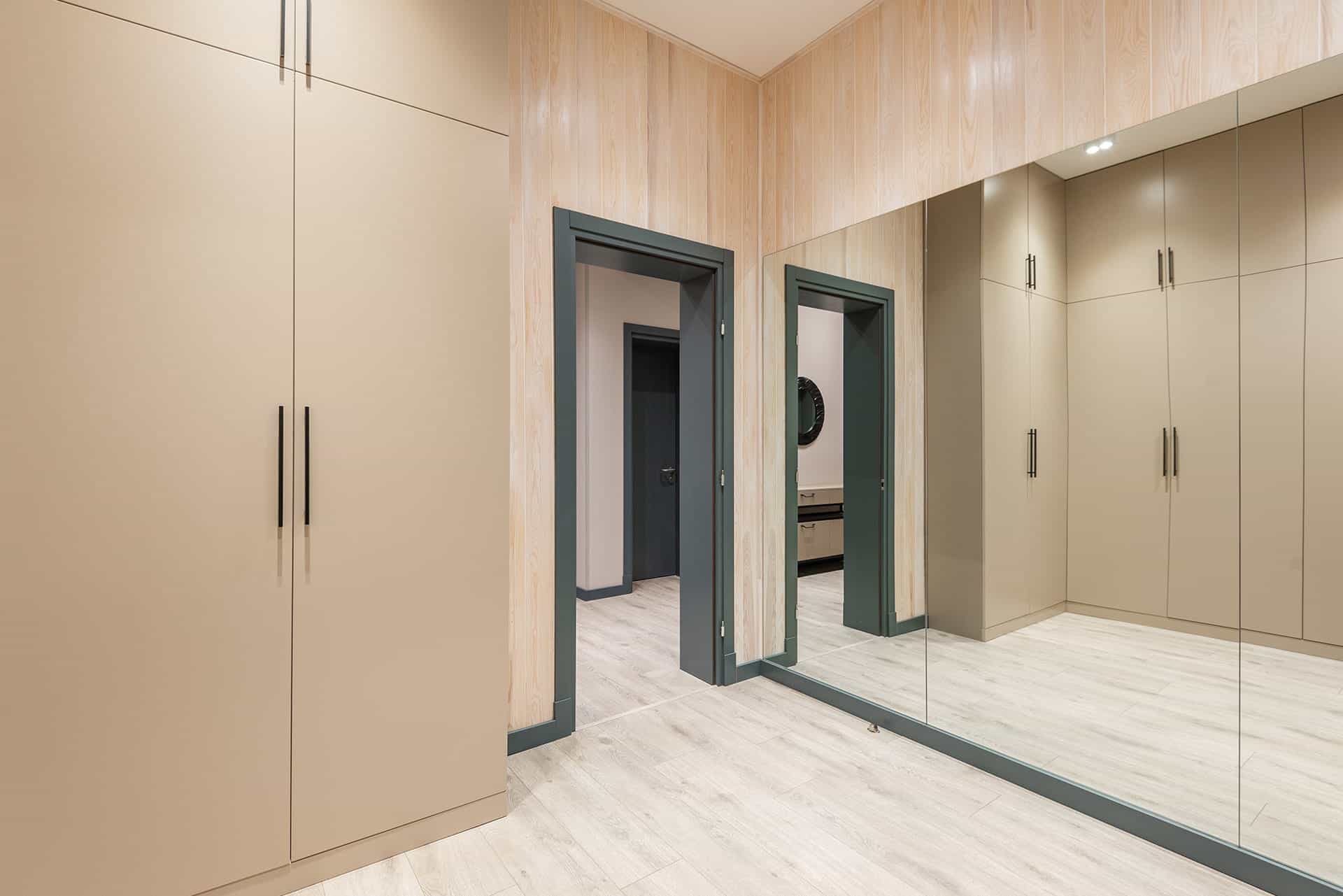 Walk-in closet with beige cabinetry, a mirrored wall, and dark gray doorway frames on a light wood floor.
